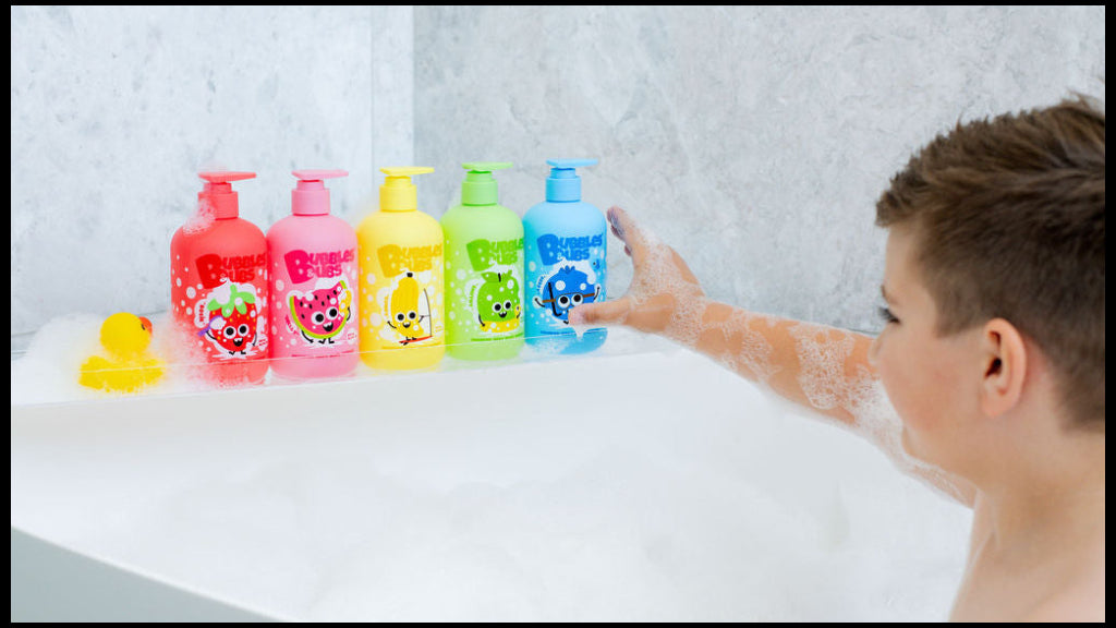 Child reaching for a colorful Berry the blueberry shampoo of bubble bath in a bathtub with the whole range of colourful shampoo bottles and duck bath toy